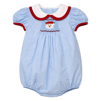 A baby romper in light blue with a white Peter Pan collar trimmed in red, featuring red trim on the sleeves and a smocked Santa face motif on the chest.