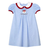 A light blue baby dress with a white Peter Pan collar trimmed in red, featuring short puff sleeves and a smocked Santa face motif at the center chest.