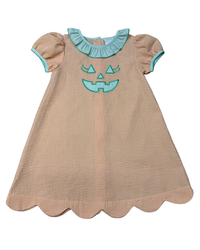 A toddler girl's dress featuring a beige and white gingham pattern, a scalloped hem, short puff sleeves with light blue trim, and a light blue ruffled collar. The front is decorated with a light blue embroidered jack-o'-lantern face.